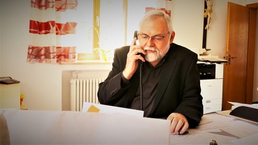 Pfarrer Martin Neidl telefoniert im Pfarrbüro.  | Bild: BR